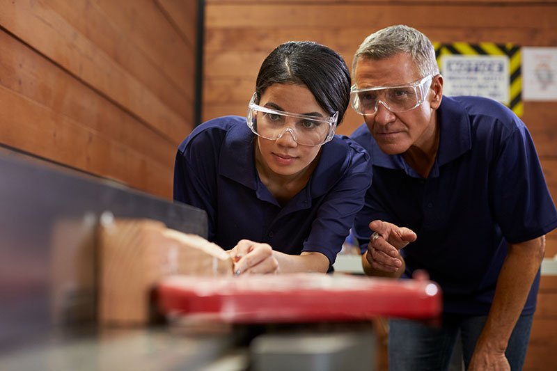 older man showing young female how to use a table saw